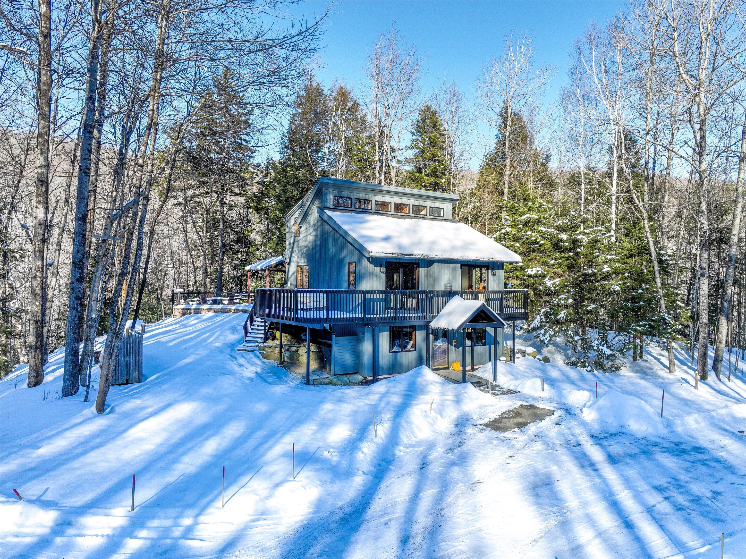A two-story cabin with a balcony, surrounded by snow-covered ground and trees.