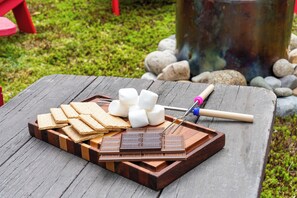 Un plateau en bois contenant des guimauves, des barres de chocolat et des biscuits Graham, posé sur une table en bois.