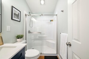 Une salle de bain moderne avec une douche à parois de verre, des toilettes blanches, un lavabo avec un plan de travail blanc et une plante en pot.