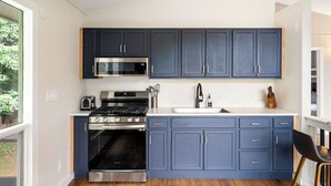 A modern kitchen with dark blue cabinets, stainless steel appliances, and a wooden floor. - Secluded Luxury Escape, Hot Tub, Fire Pit, Game Room & Yoga, Walk to Town (Woodstock)