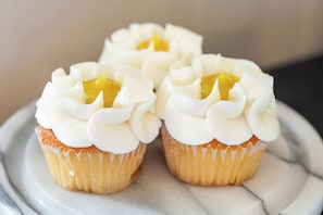 Trois petits gâteaux décorés d’un glaçage blanc et garnis d’une crème jaune, présentés sur une surface en marbre.