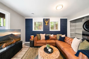 A modern living room with a brown leather sofa, a round coffee table with a plant, and a TV on a stand.