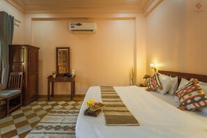 A hotel room with a bed, a desk, a chair, an air conditioning unit, and a nightstand with a lamp. - Eartham Stays Pushkar (Pushkar)