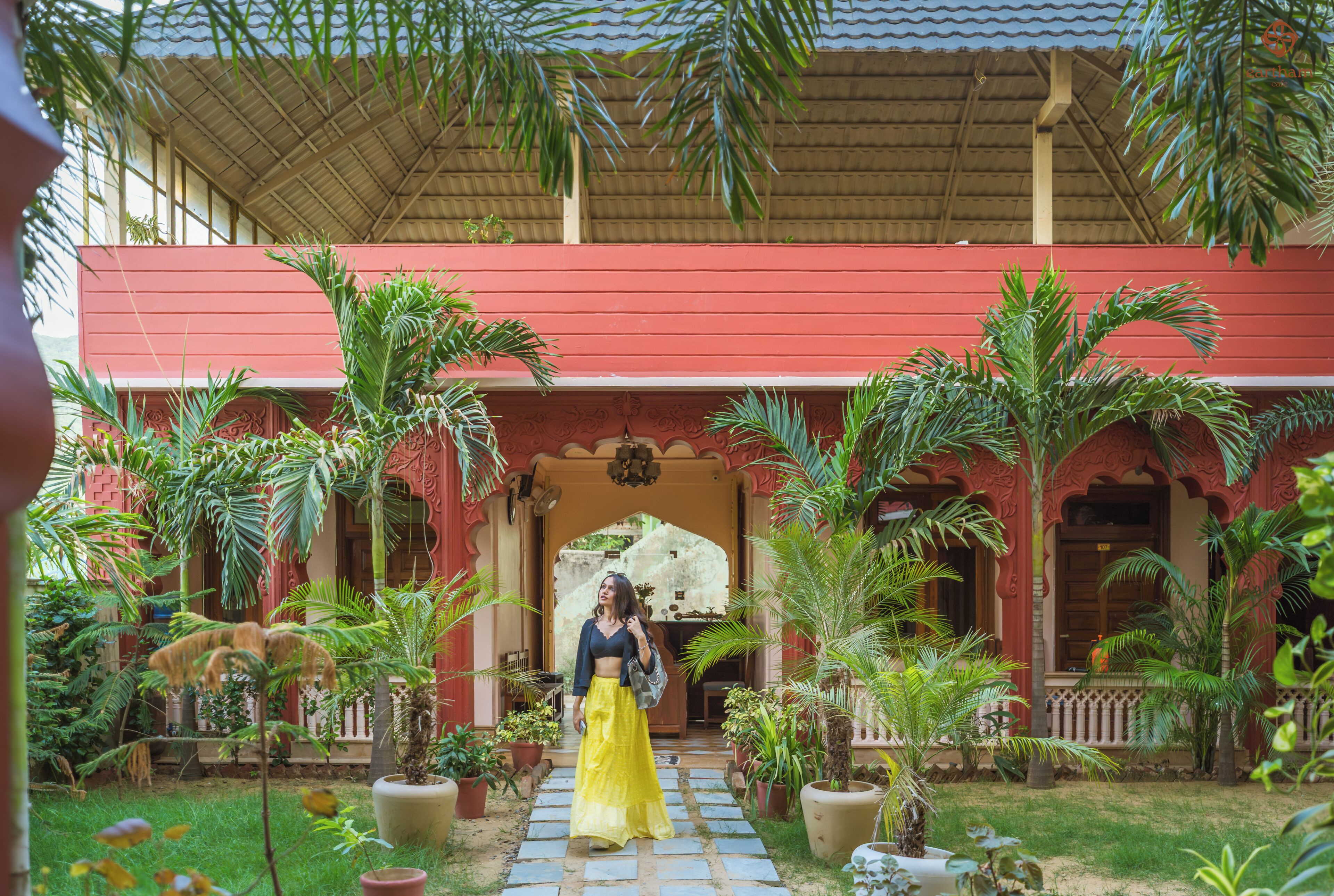 A covered outdoor area with a red building, potted plants, and a pathway.