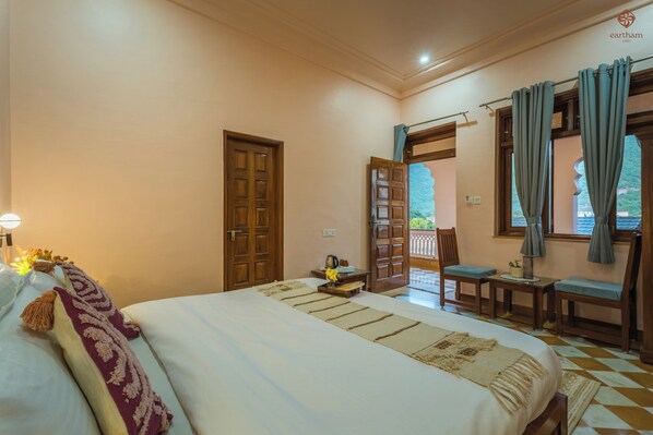 Habitación de hotel con cama, escritorio, silla, ventana con cortinas y vista a zonas verdes.
