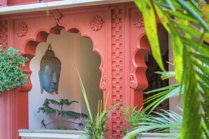 A Buddha statue mounted on a wall with intricate carvings, surrounded by greenery and architectural details. - Eartham Stays Pushkar (Pushkar)