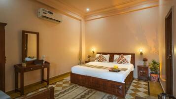 Habitación de hotel con cama, mesita de noche, espejo, equipo de aire acondicionado y una pequeña planta en maceta.