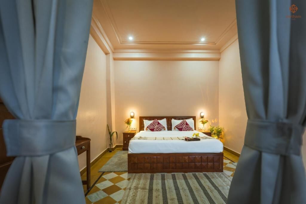 Habitación de hotel con cama, lámparas de noche, mesita de noche y alfombra estampada.