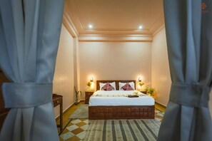 Quarto de hotel com cama, abajures, mesa de cabeceira e tapete estampado.