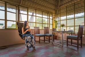 Una habitación con una hamaca, sillas de madera, una mesa y grandes ventanas que ofrecen vistas del exterior.