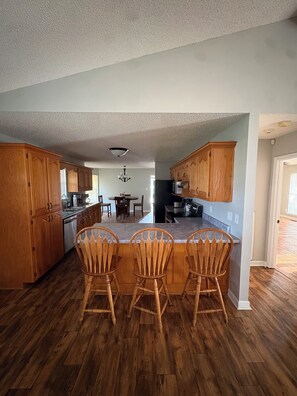 A kitchen with wooden cabinets, a dining area with chairs, and a central island with chairs. -  Can hunt on TVA land  Hunters and Fishermans Guntersville Getaway   3BR • 2BA (Langston)