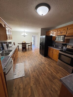 A kitchen with wooden cabinets, a refrigerator, a microwave, and a dining table with chairs. -  Can hunt on TVA land  Hunters and Fishermans Guntersville Getaway   3BR • 2BA (Langston)