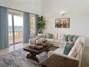 A living room with a sofa, coffee table, and a painting on the wall. - Luxury Oceanfront Villa in Anguilla with breathtaking Atlantic Ocean Views. (Island Harbour)