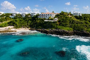 A coastal property with a beach, clear turquoise waters, and a large white building with multiple balconies. - Luxury Oceanfront Villa in Anguilla with breathtaking Atlantic Ocean Views. (Island Harbour)