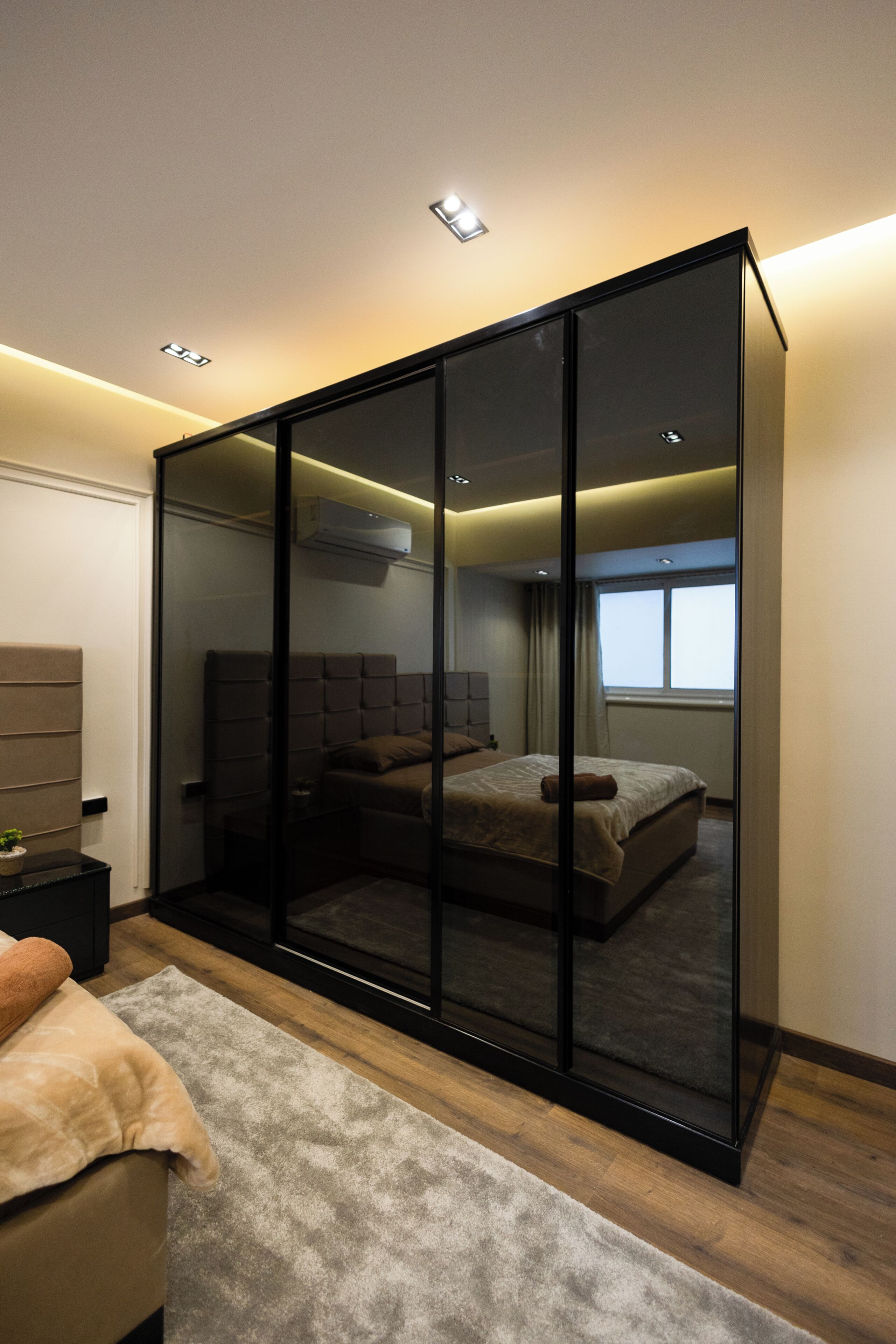 Une chambre moderne avec un placard à portes coulissantes en verre, un lit avec une tête de lit, une table de chevet et une fenêtre avec des rideaux.
