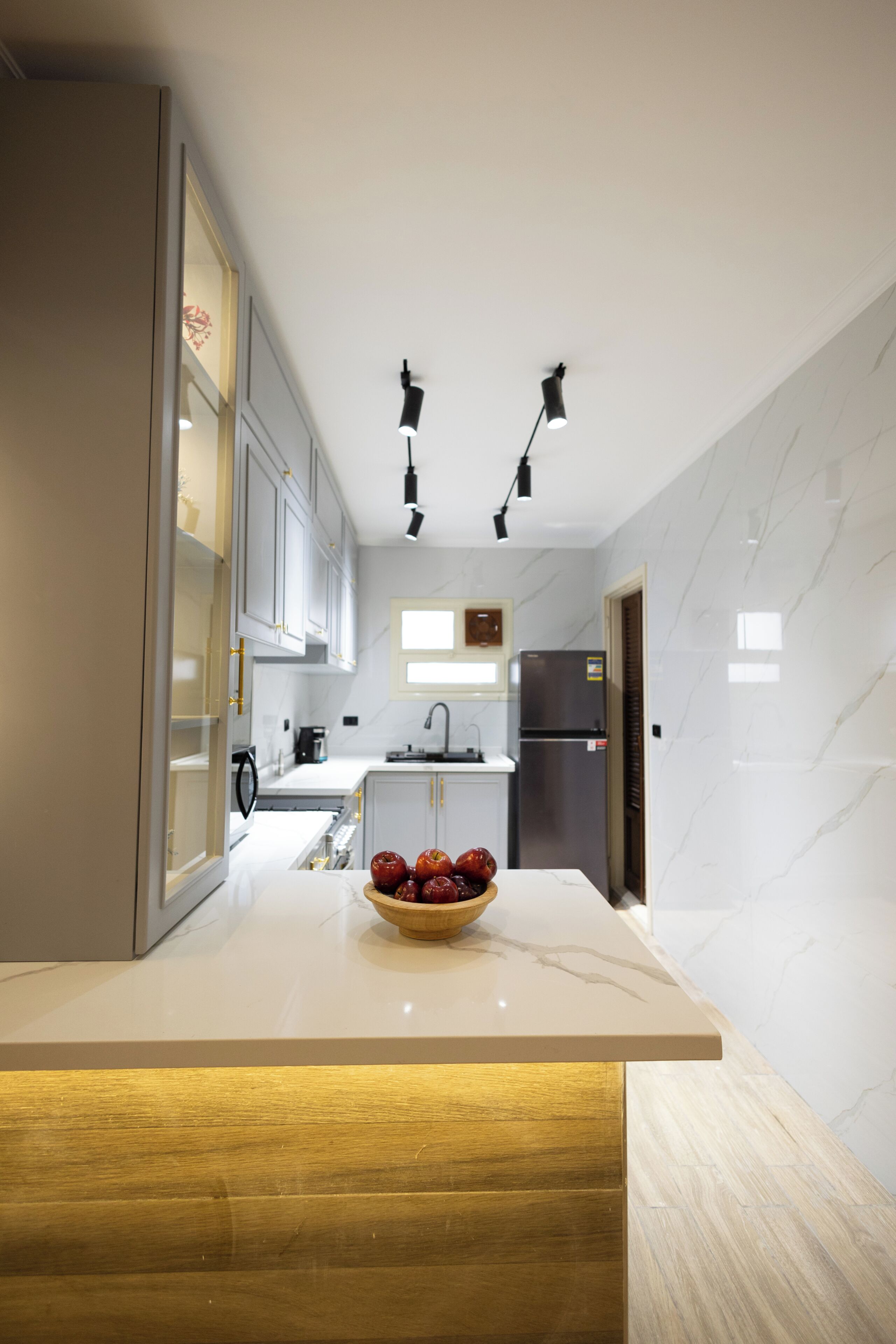 Una cocina moderna con encimera de mármol, un cuenco de fruta y un refrigerador de acero inoxidable.