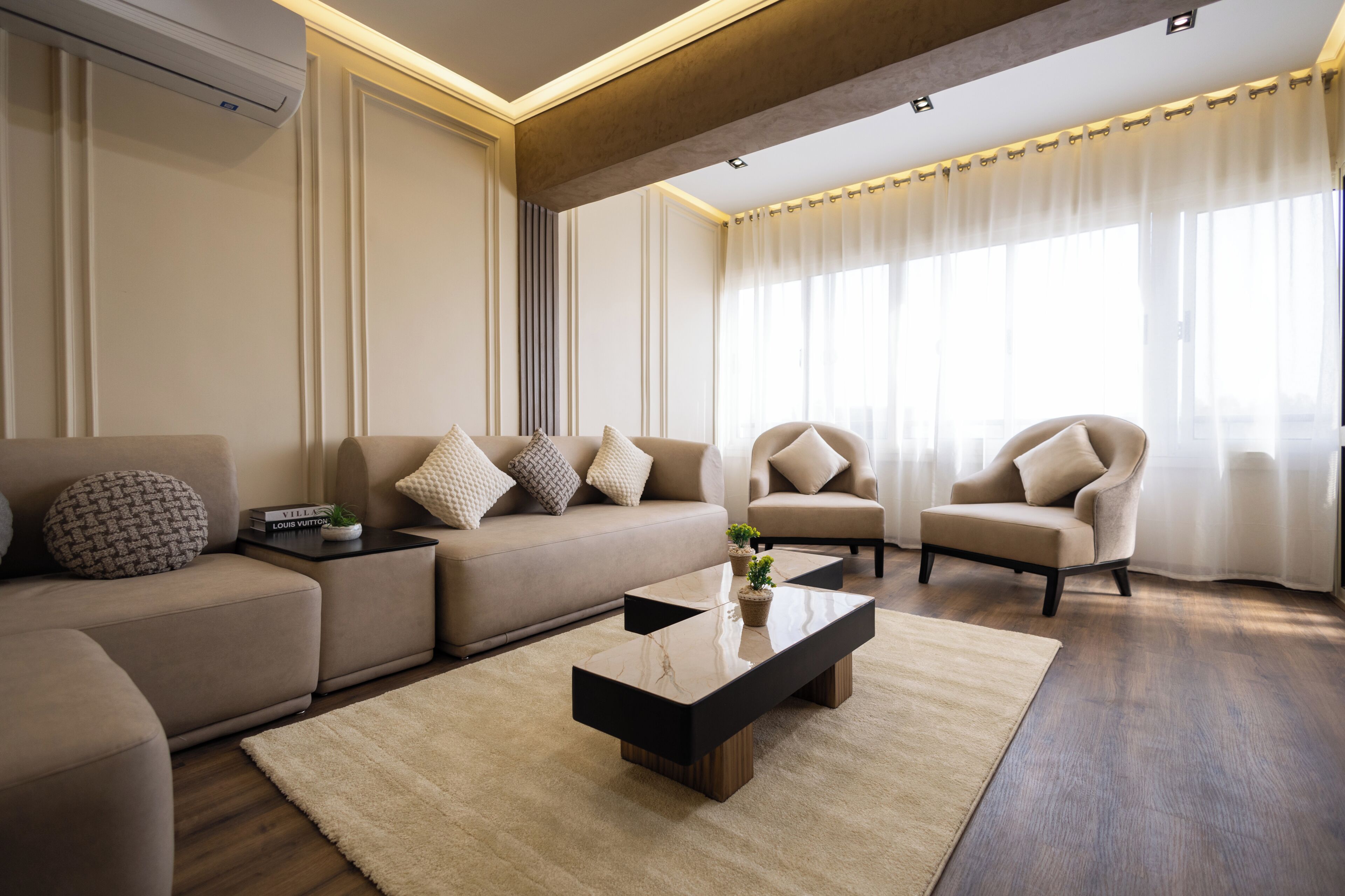 Una sala de estar moderna con sofá, sillones, una mesa de centro y un amplio ventanal con cortinas.
