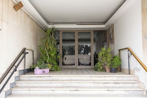 Un conjunto de escalones exteriores que conducen a la entrada de un edificio con puertas de cristal, rodeado de plantas en macetas.