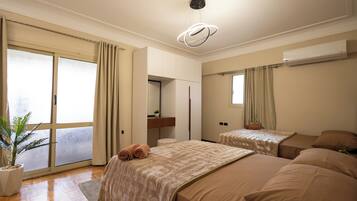 Habitación de hotel con un gran ventanal corredero, una cama con una manta color crema, una mesita de noche pequeña con una planta y una lámpara de techo.