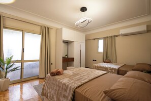 A hotel room with a large sliding door, a bed with a beige blanket, a small bedside table with a plant, and a ceiling light fixture.