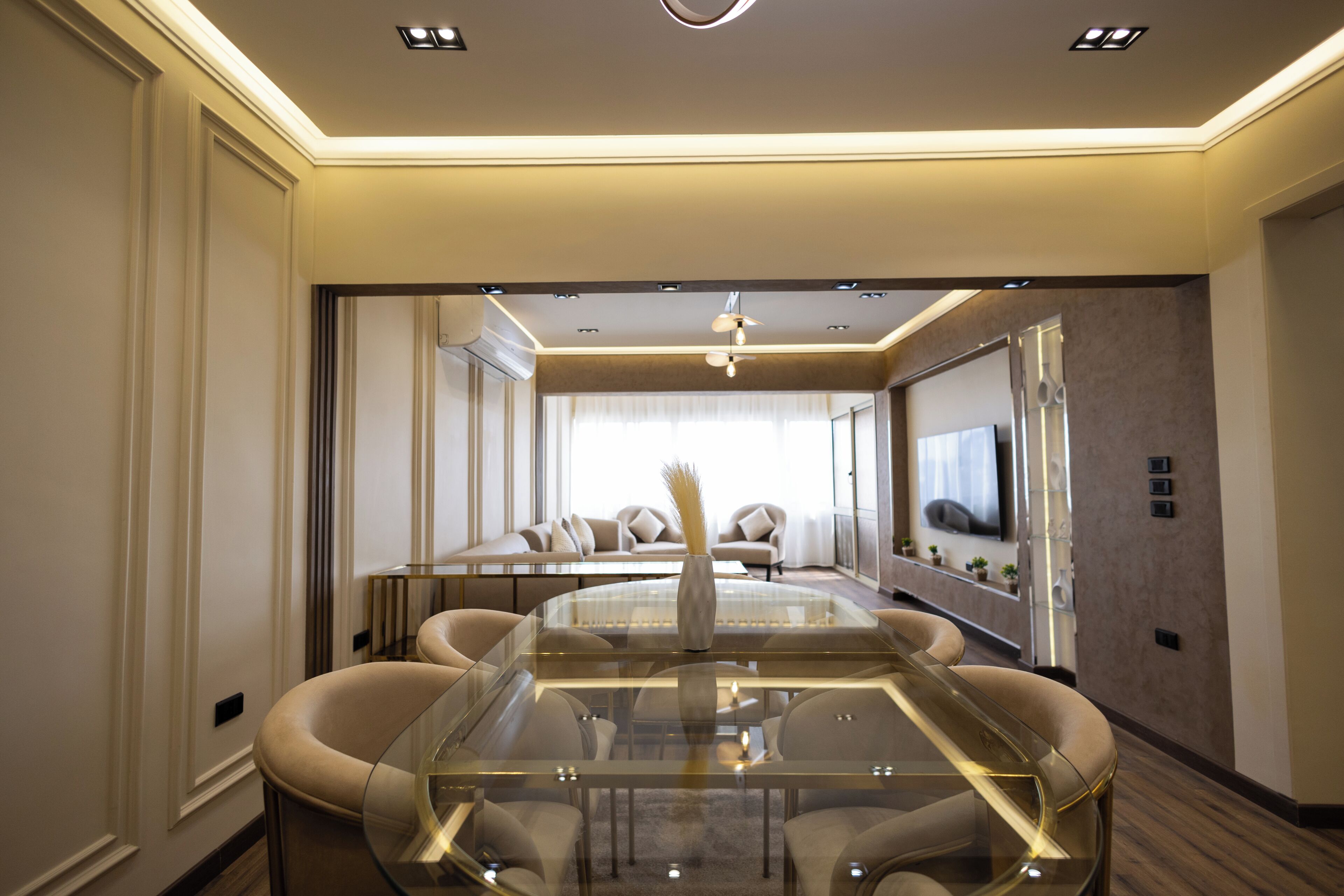 Une chambre d’hôtel moderne dotée d’une table à manger en verre, de sièges confortables, d’un téléviseur à écran plat et d’une grande fenêtre.