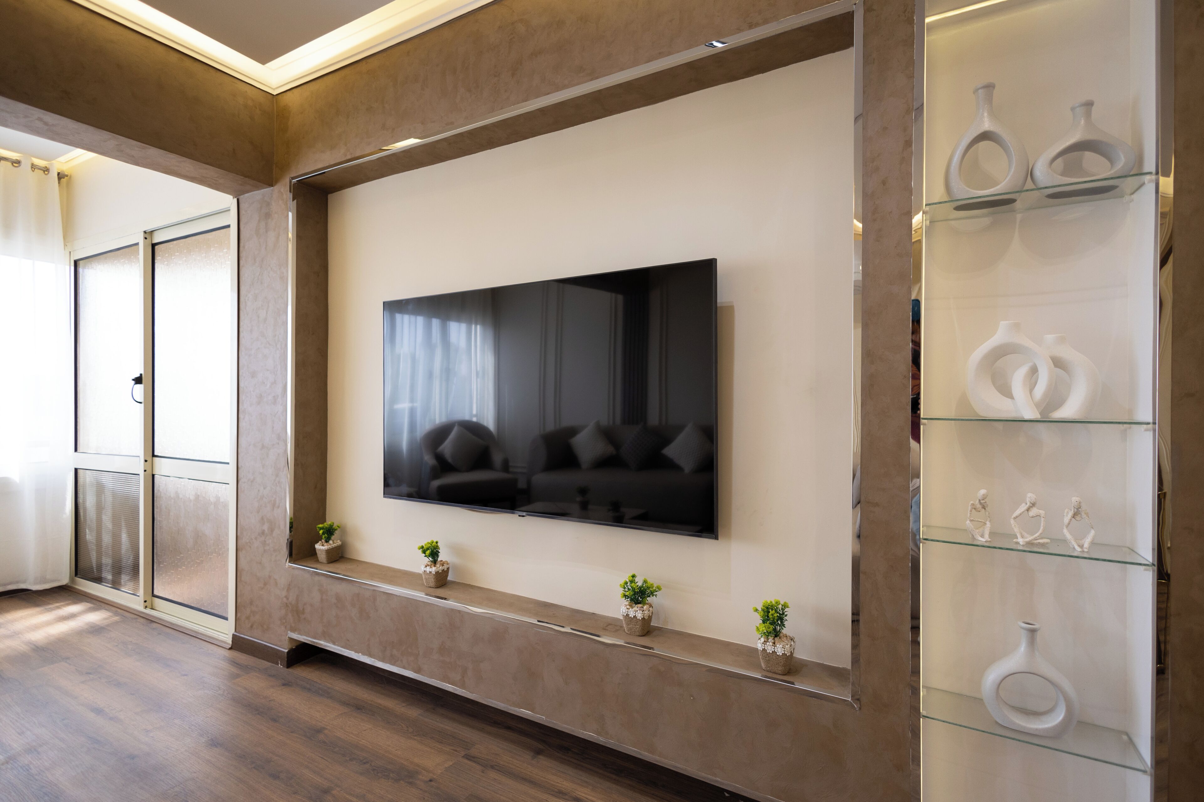 Un salon moderne doté d’un grand téléviseur à écran plat fixé au mur, d’une vitrine en verre contenant des objets décoratifs et d’un plancher en bois.