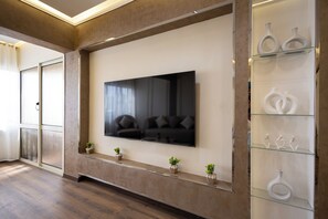 A modern living room with a large flat-screen TV mounted on a wall, a glass display cabinet with decorative items, and a wooden floor.