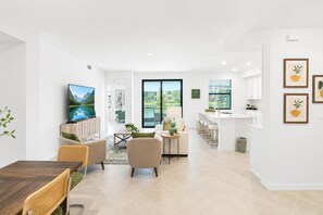 A modern living room with a flat-screen TV, a dining area with a wooden table, and a kitchen with a bar. - Sun Seeker Lakefront Condo (Bradenton)