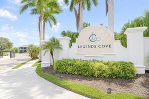 A sign for Legends Cove with a landscaped entrance featuring palm trees and a hedge. - Sun Seeker Lakefront Condo (Bradenton)