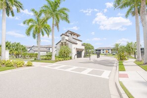A residential street with palm trees, a gated entrance, and houses with a Mediterranean architectural style. - Sun Seeker Lakefront Condo (Bradenton)