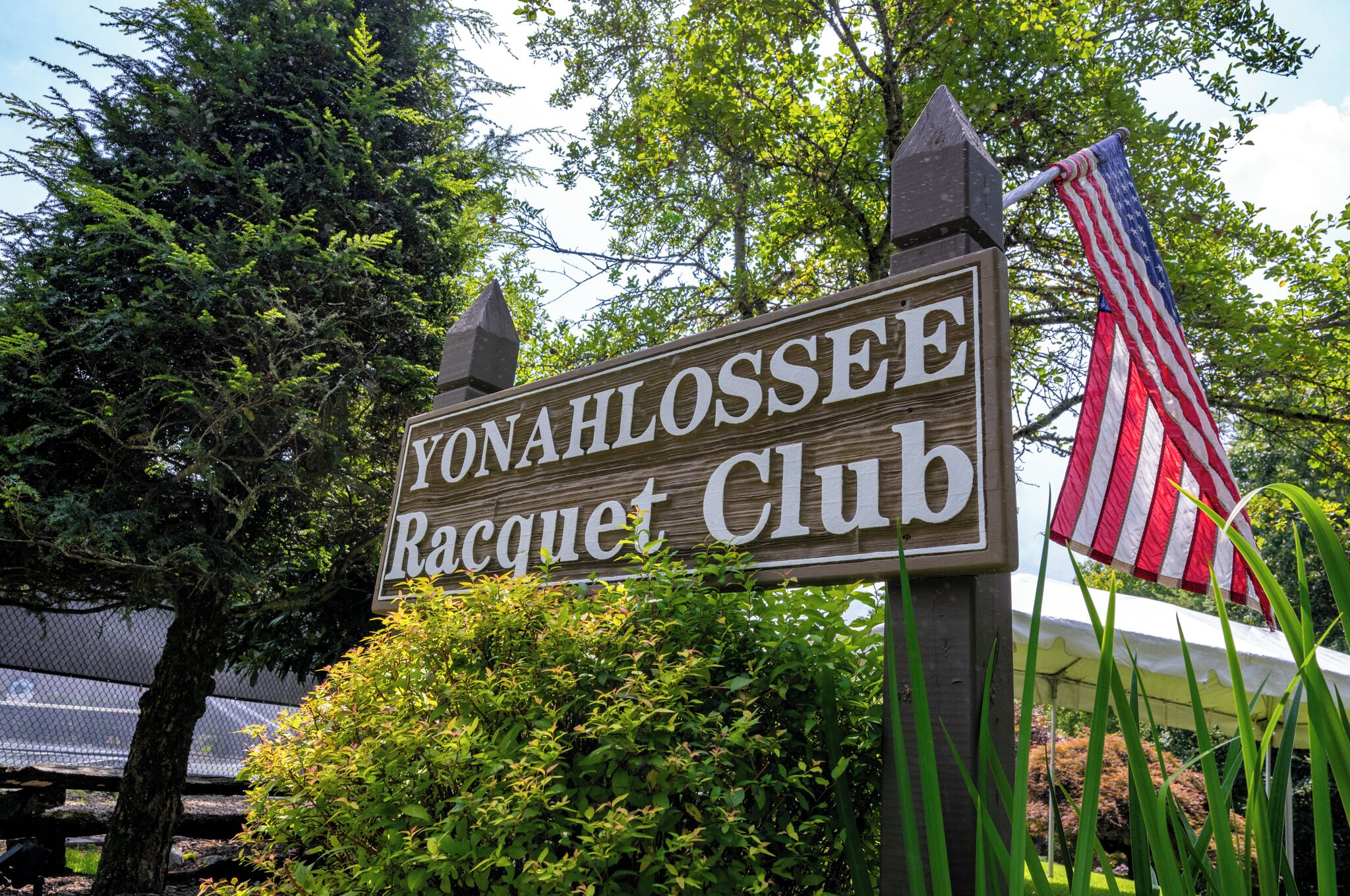 Ein Holzschild mit der Aufschrift 'YONAHLOSSEE Racquet Club' und einer amerikanischen Flagge.