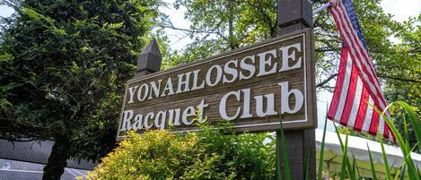 Ein Holzschild mit der Aufschrift 'YONAHLOSSEE Racquet Club' und einer amerikanischen Flagge.