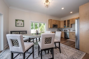 A modern kitchen with wooden cabinets, a stainless steel refrigerator, and a dining area with a round table and chairs. - 01 Blue Ridge Mountains View - House & Resort (Boone)