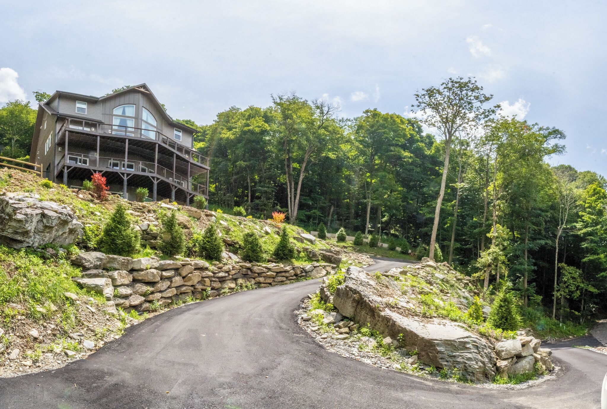 A multi-level house with a stone retaining wall and a winding road.