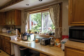 A kitchen with wooden cabinets, a window with curtains, and various appliances like a toaster and a kettle.