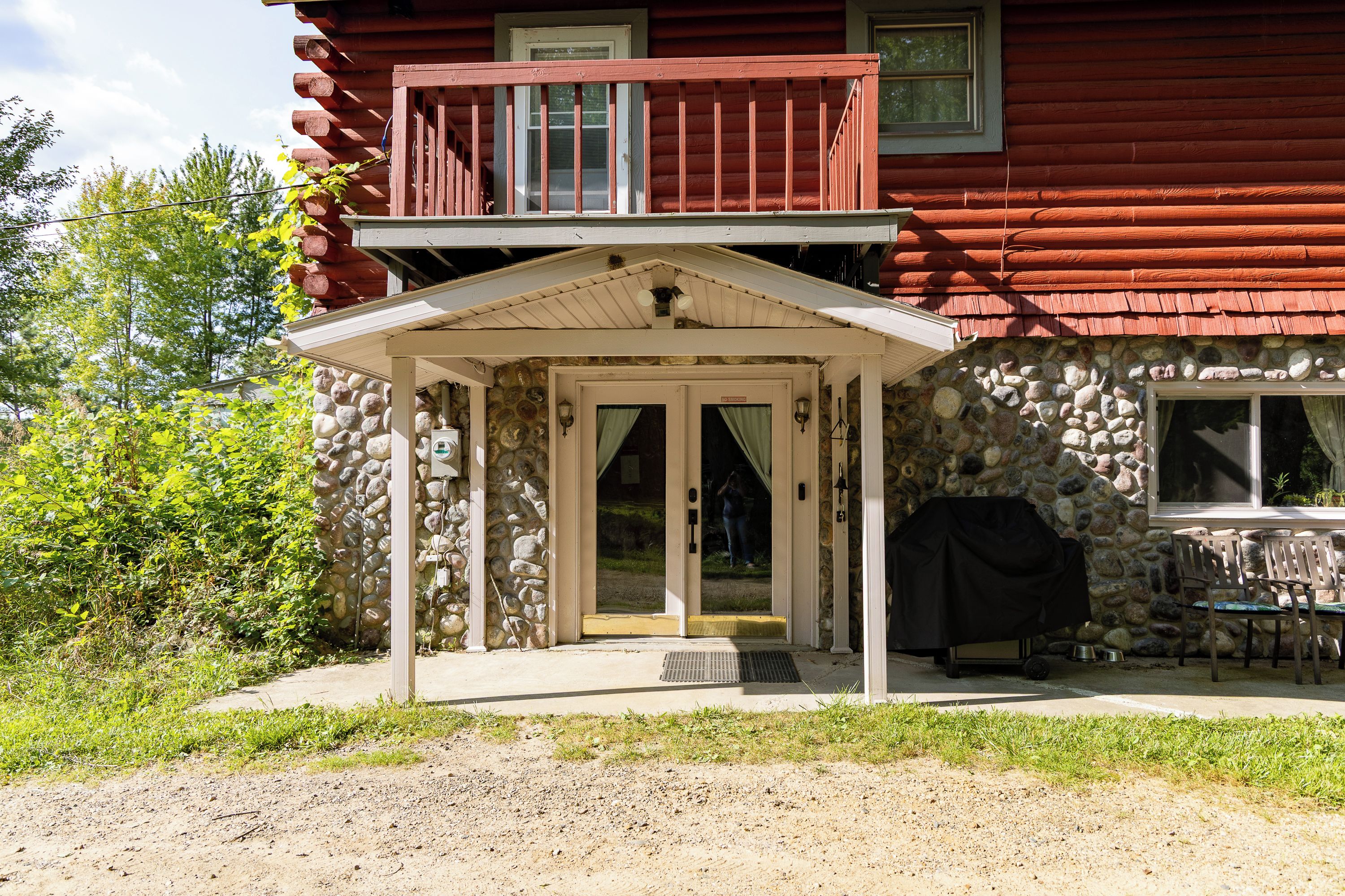 Eine zweistöckige Holzhütte mit Steinfundament, einer Veranda und einem kleinen Sitzbereich im Freien.