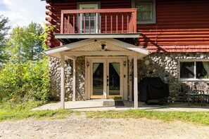 Eine zweistöckige Holzhütte mit Steinfundament, einer Veranda und einem kleinen Sitzbereich im Freien.