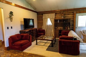 A living room with a television, red sofas, a glass coffee table, and a wooden bookshelf.