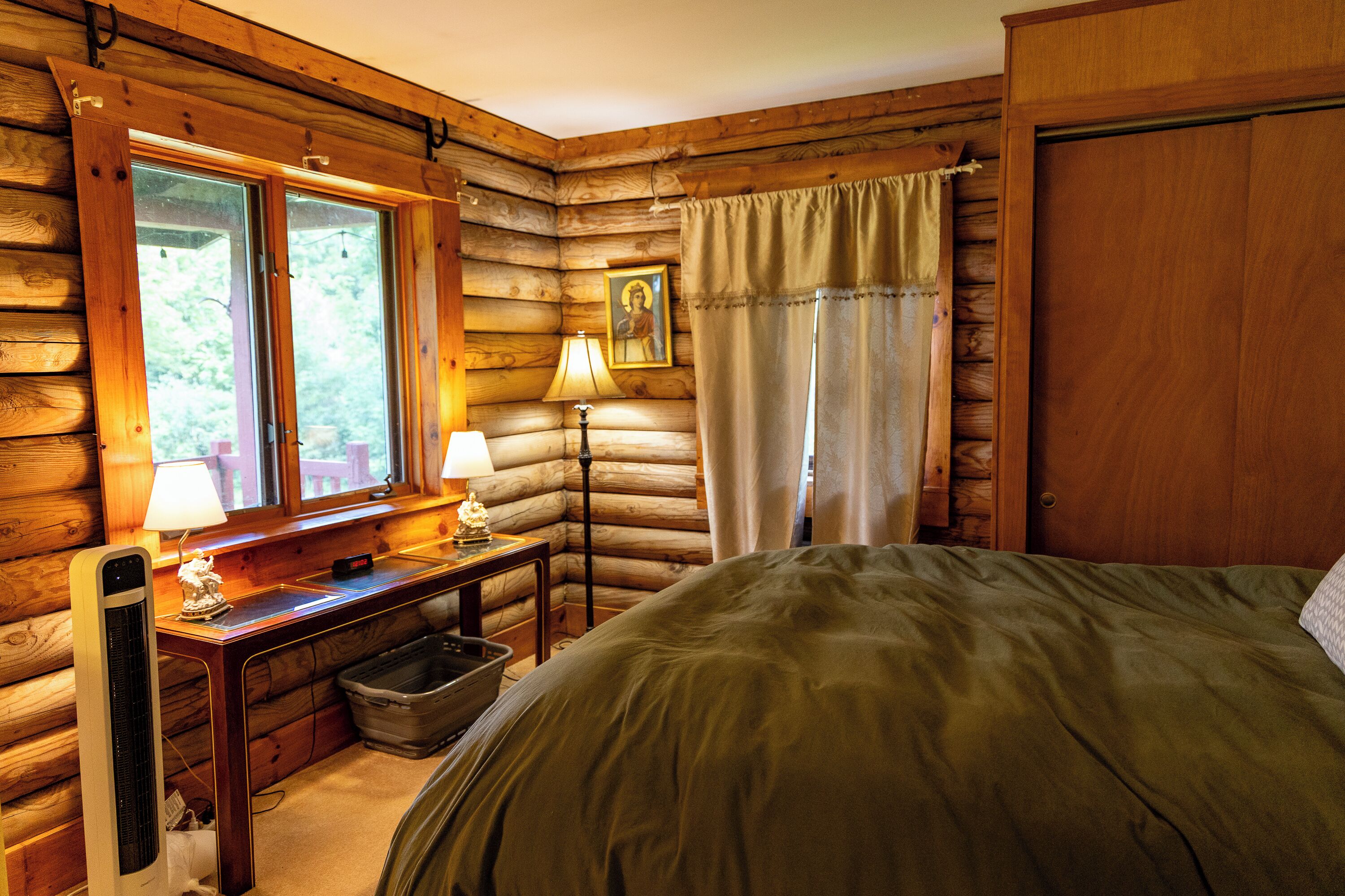 Ein Schlafzimmer in einer Blockhütte mit einem Bett, zwei Nachttischlampen, einem Nachttisch, einem Fenster und einer Tür.