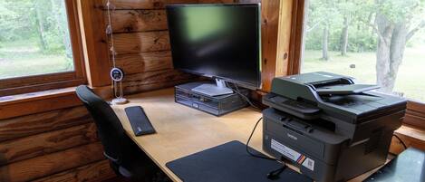 Een houten bureau, een computer, een printer en een stoel in een chalet.