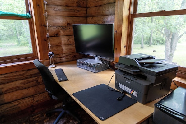 El interior de una cabaña con un escritorio de madera, una computadora, una impresora y una silla.