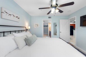 A bedroom with a bed, a ceiling fan, a nightstand, and a wall-mounted artwork. - Renovated Top-Floor Clearwater Condo | Quiet, King Bed, Sleeps 4, Heated Pool & Gym (Clearwater)