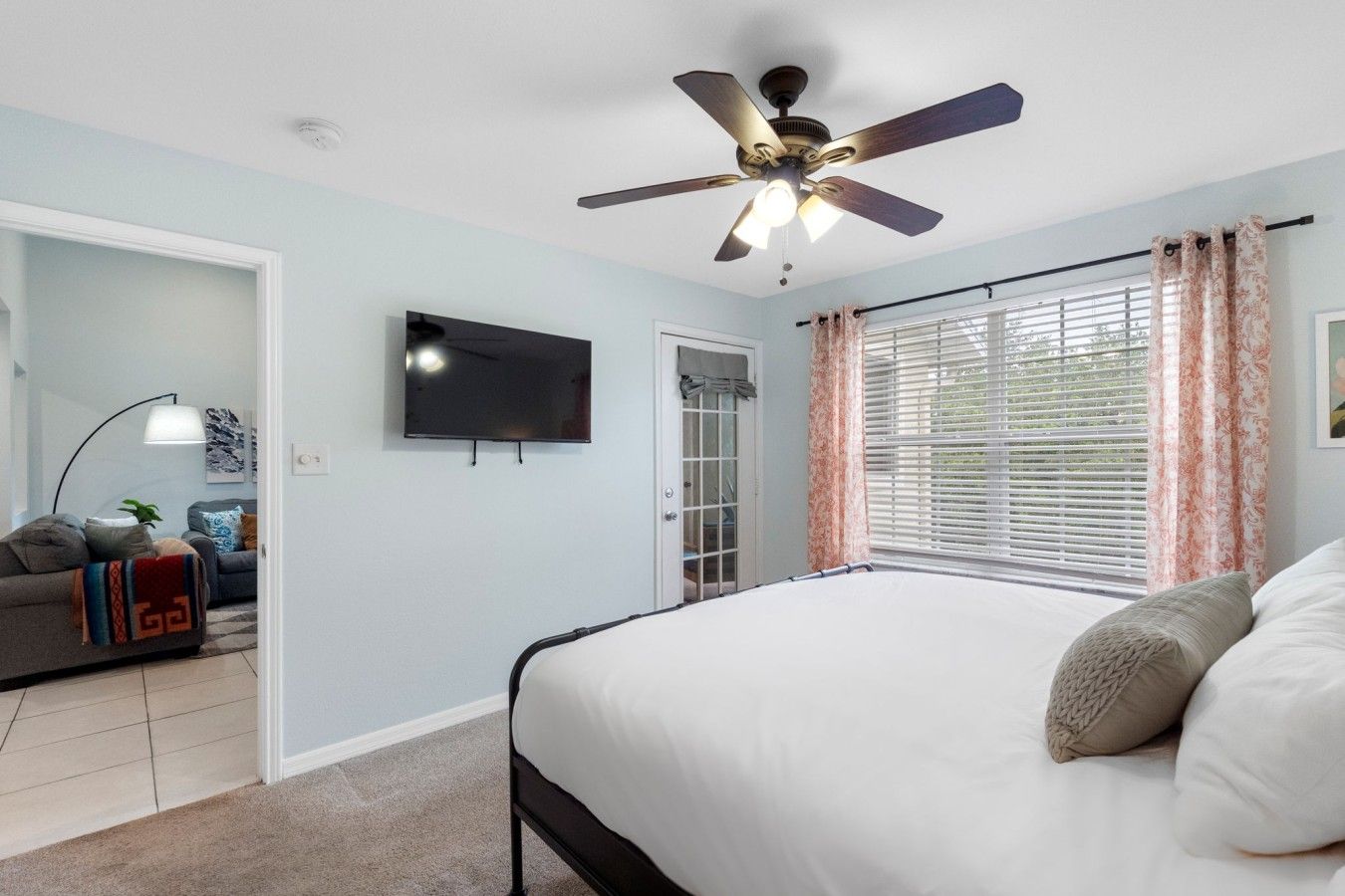 Une chambre à coucher avec un lit, un ventilateur de plafond, une télévision et une fenêtre avec des rideaux.