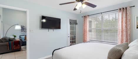 Un dormitorio con cama, ventilador de techo, televisor y ventana con cortinas.