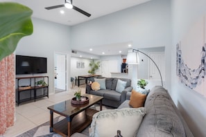 A modern living room with a sofa, coffee table, TV, and a dining area with chairs and a table. - Renovated Top-Floor Clearwater Condo | Quiet, King Bed, Sleeps 4, Heated Pool & Gym (Clearwater)