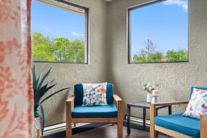 A corner room with two windows, a wooden chair with a blue cushion, a small table, and a potted plant. - Renovated Top-Floor Clearwater Condo | Quiet, King Bed, Sleeps 4, Heated Pool & Gym (Clearwater)