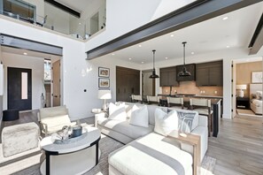 A spacious living area with a sofa, coffee table, and a dining area with chairs and a kitchen in the background. - Spacious 5BR Canyons Retreat with Hot Tub Near Park City Mountain (Park City)