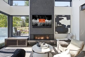 A modern living room with a fireplace, a television mounted on the wall, and a view of the outdoors. - Spacious 5BR Canyons Retreat with Hot Tub Near Park City Mountain (Park City)