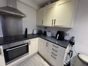 A kitchen with white cabinets, a black countertop, a built-in oven, and a coffee maker.