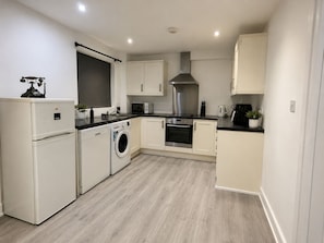 A compact kitchen with a washing machine, oven, microwave, and a large window.